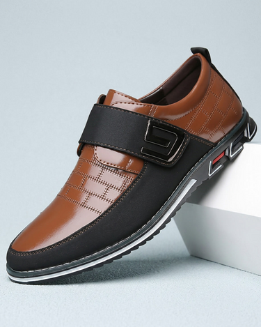 Brown and black shoe with a strap on a light gray background