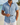 Camicia uomo azzurra a manica corta con bottoni a vista, colletto a revers, su spiaggia.