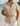 Camicia uomo beige a manica corta con bottoni, colletto a revers, tessuto testurizzato, su spiaggia.
